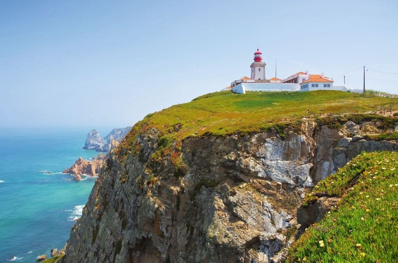 Leuchtturm auf Klippe am Cabo da Roca, Portugal, mit blauem Meer im Hintergrund.