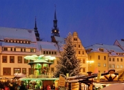 Verschneiter Weihnachtsmarkt am Abend mit historischen Gebäuden und Weihnachtsbaum.