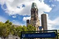 Gedächtniskirche in Berlin am Kurfürstendamm bei klarem Himmel und U-Bahn-Schild im Vordergrund.