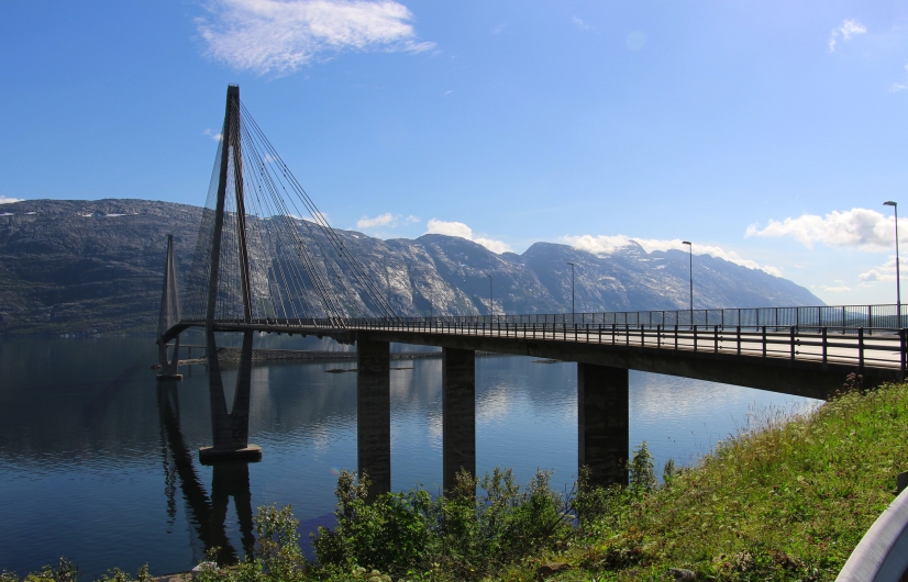 Hängebrücke über einen ruhigen See mit Bergen im Hintergrund