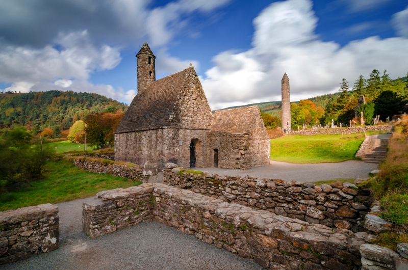 Steinernes Gebäude mit Turm in grüner Landschaft unter bewölktem Himmel.
