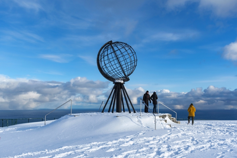 Menschen stehen bei winterlicher Aussicht an der Nordkapp-Globe-Skulptur in Norwegen.