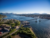 Luftaufnahme einer Brücke über eine Küstenlandschaft mit Bergen im Hintergrund.