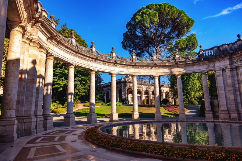 Historischer Säulengang mit Rundbogen und Wasserbecken im Sonnenschein.