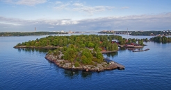 Kleine bewaldete Insel in einem großen Gewässer mit Häusern und Steg.
