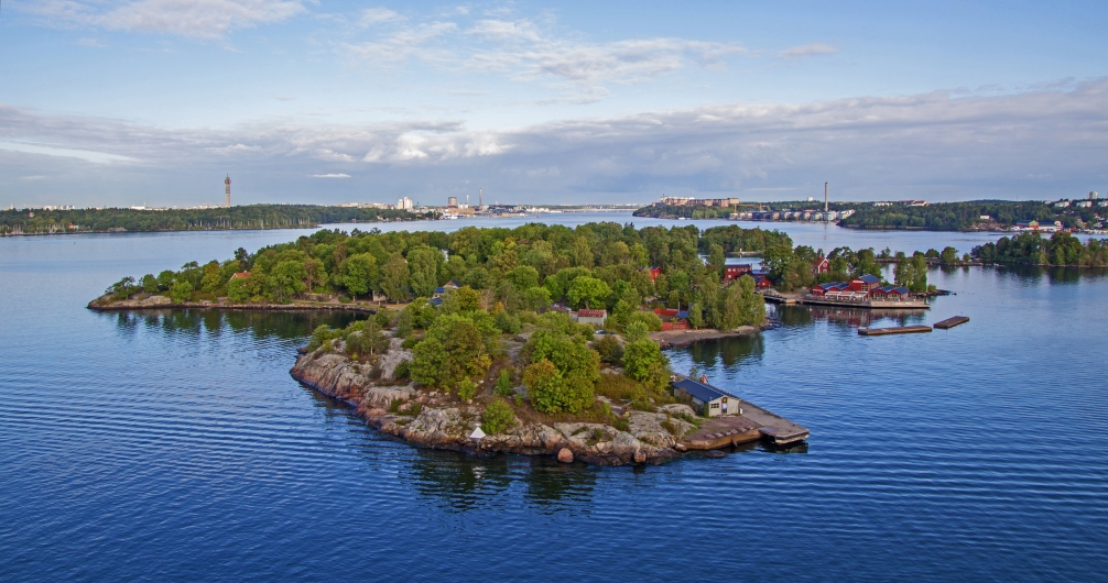 Kleine bewaldete Insel in einem großen Gewässer mit Häusern und Steg.