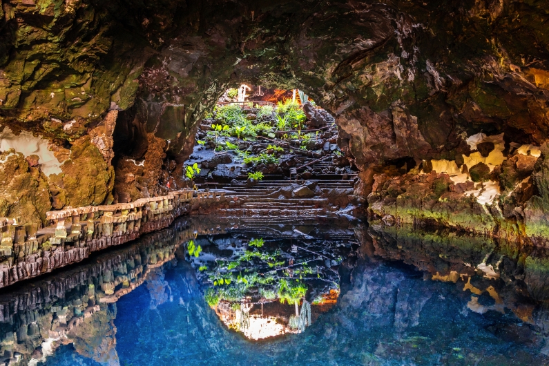 Unterirdische Höhle mit blauem Wasser und Pflanzen an den Felswänden.