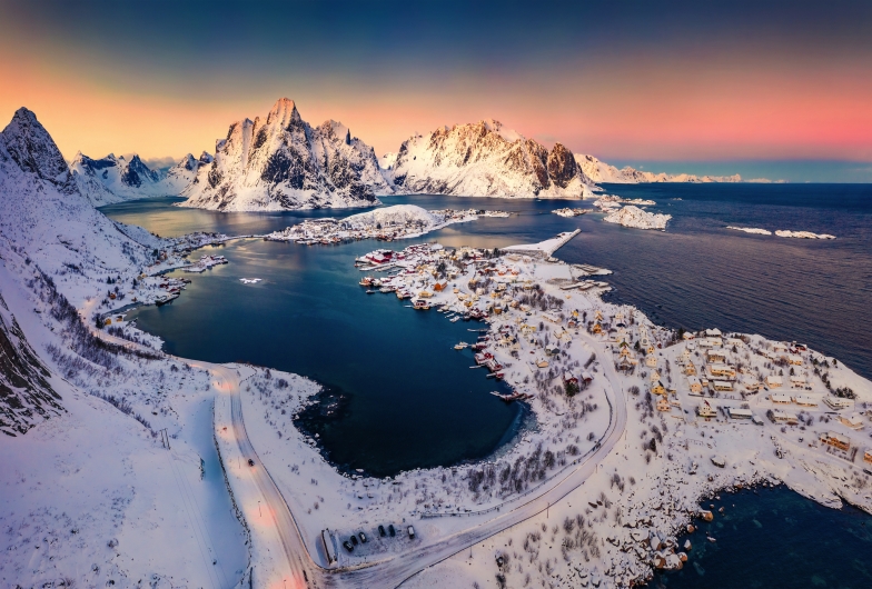 Winterliche Landschaft mit verschneiten Bergen und einem fjordähnlichen See bei Sonnenuntergang.