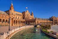 Plaza de España in Sevilla bei sonnigem Wetter mit Wasserkanal und Booten im Vordergrund.