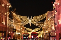 Weihnachtlich beleuchtete Einkaufsstraße mit Engelsdekoration und roten Doppeldeckerbussen.
