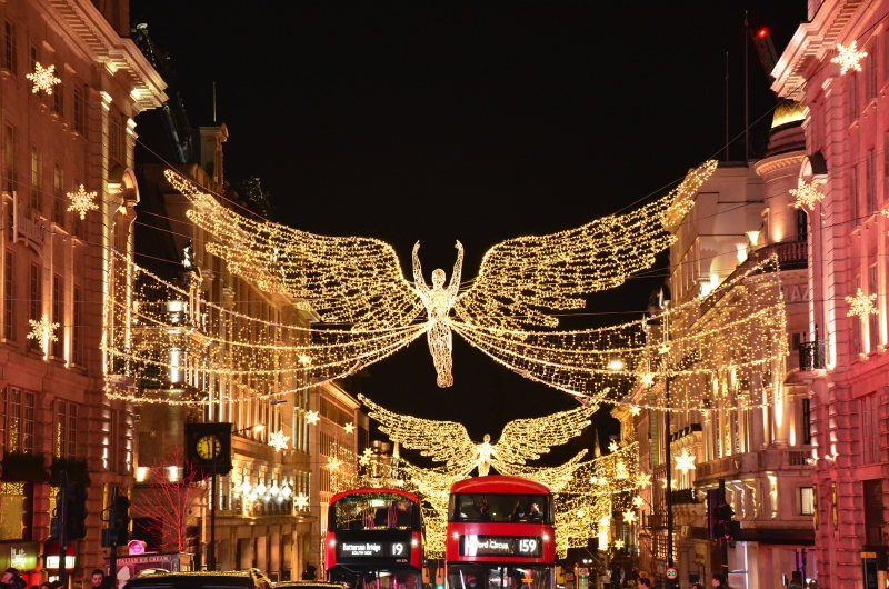 Weihnachtlich beleuchtete Einkaufsstraße mit Engelsdekoration und roten Doppeldeckerbussen.