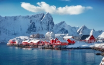 Verschneite Holzhäuser am Fjord vor schneebedeckten Bergen in Norwegen.