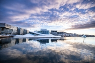 Opernhaus in Oslo, reflektiert im Wasser, mit blauem Himmel und Wolken.