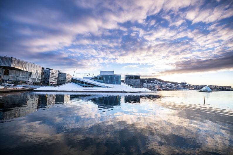 Opernhaus in Oslo, reflektiert im Wasser, mit blauem Himmel und Wolken.
