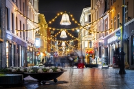 Beleuchtete, festlich geschmückte Straßenszene bei Nacht mit verschwommenen Spaziergängern.