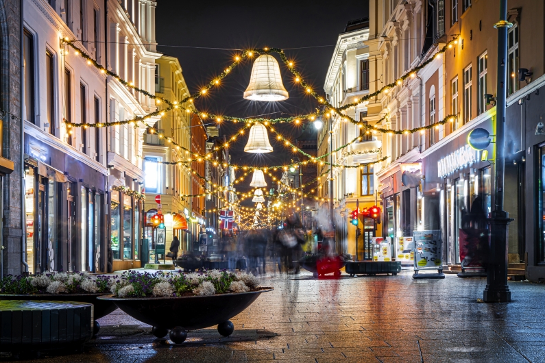 Beleuchtete, festlich geschmückte Straßenszene bei Nacht mit verschwommenen Spaziergängern.