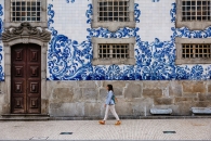 Person spaziert vor einer Fliesenfassade mit blauen Mustern.