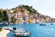 Küstenstadt mit Hafen und befestigtem Hügel im Hintergrund.