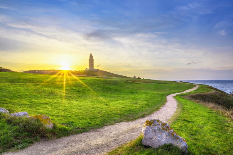 Leuchtturm am Horizont, umgeben von grünen Wiesen, bei Sonnenuntergang.