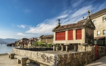 Traditionelle galicische Getreidespeicher auf Stelzen mit Kreuz auf dem Dach, direkt am Ufer der Ría de Pontevedra im Fischerort Combarro, im Hintergrund das ruhige Wasser der Bucht.