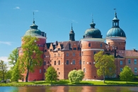 Historisches Schloss mit runden Türmen vor blauem Himmel und Bäumen im Vordergrund.