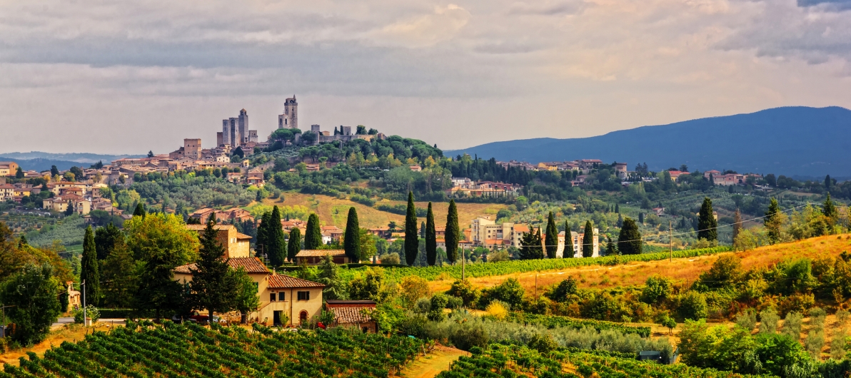 Hügelige Landschaft mit historischen Türmen und Weinbergen in der Toskana.