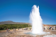 Ein Geysir bricht aus, umgeben von Menschen unter blauem Himmel.