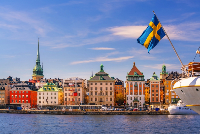 Blick auf Stockholm mit Gebäuden und schwedischer Flagge bei sonnigem Wetter.