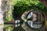 Kanal mit Brücken und Pflanzen, sonniger Tag, ruhiges Wasser.