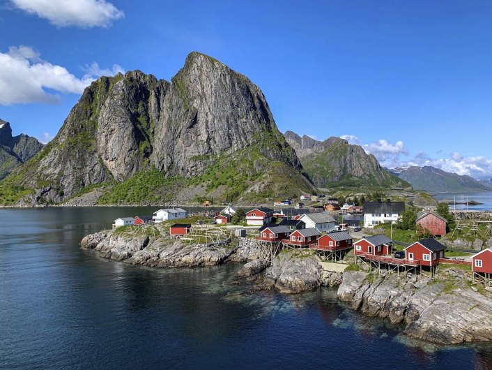 Rote Holzhäuser auf Felsen am Ufer vor Berg