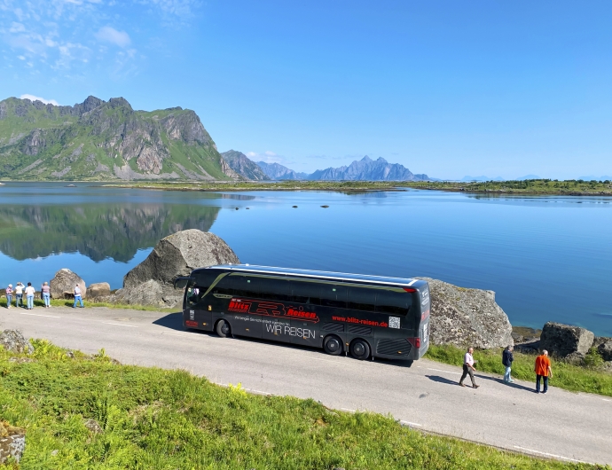 Bus mit Gästen vor blauem Gewässer mit Bergen
