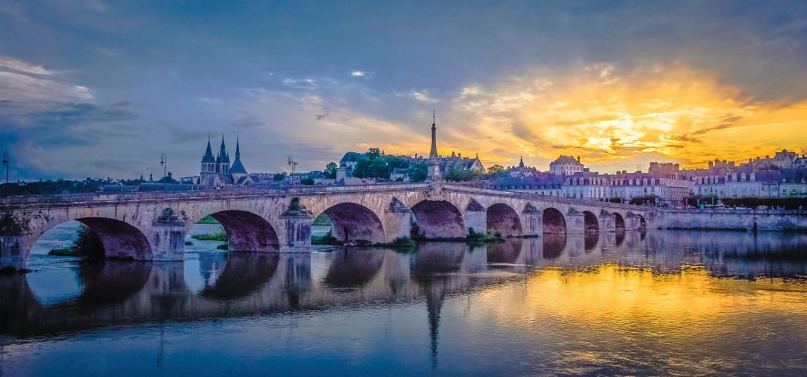 Steinbrücke über einen Fluss bei Sonnenuntergang mit reflektierendem Wasser