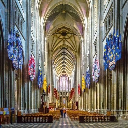 Innenraum einer großen gotischen Kathedrale mit bunten Wappen an den Wänden.