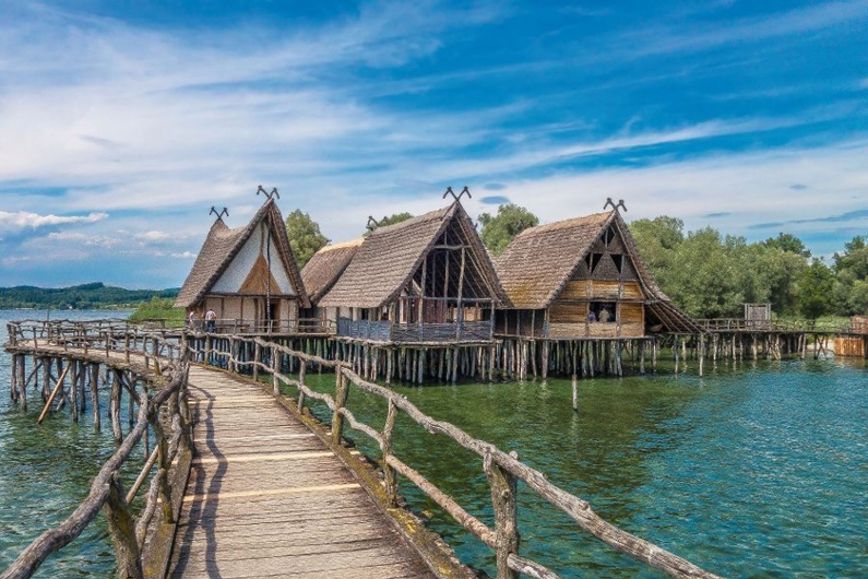 Hölzerne Pfahlbauten über Wasser mit Steg und bewölktem Himmel.