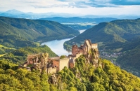 Burg auf Hügel mit bewaldeter Landschaft und Fluss im Hintergrund.