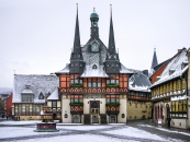 Verschneites Fachwerk-Rathaus mit Türmen und Marktbrunnen in einer Altstadt.
