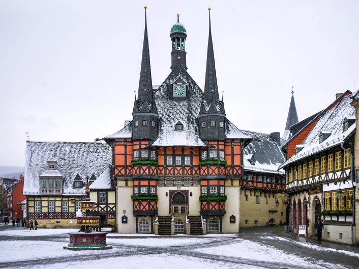 Verschneites Fachwerk-Rathaus mit Türmen und Marktbrunnen in einer Altstadt.