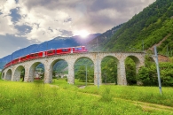 Roter Zug auf einem Viadukt in bergiger Landschaft