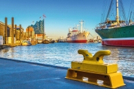 Gelber Poller am Hafen mit Schiffen und modernem Gebäude im Hintergrund.