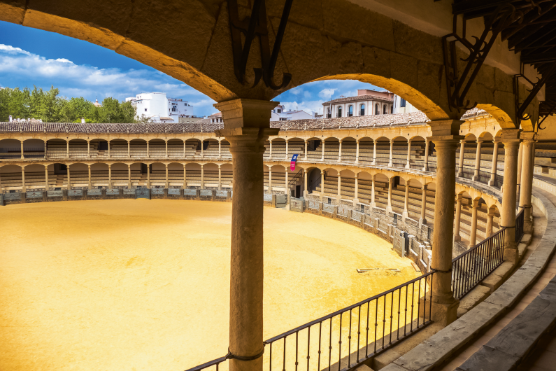 Blick in eine historische Stierkampfarena mit Säulen und Sandboden.