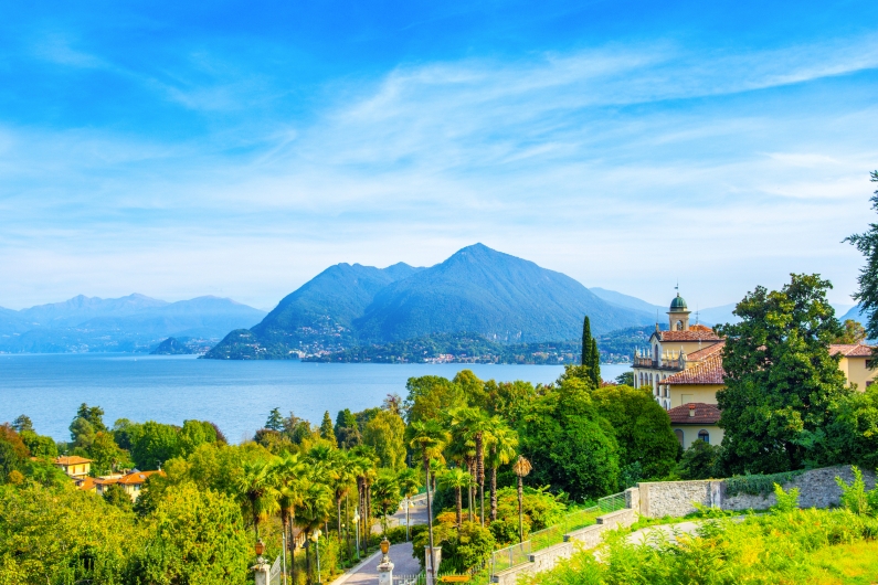 Landschaft am See mit Bergen im Hintergrund und einem Gebäude im Vordergrund.