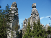Hohe, zerklüftete Felsformationen aus Sandstein umgeben von Kiefern und einem klaren blauen Himmel.