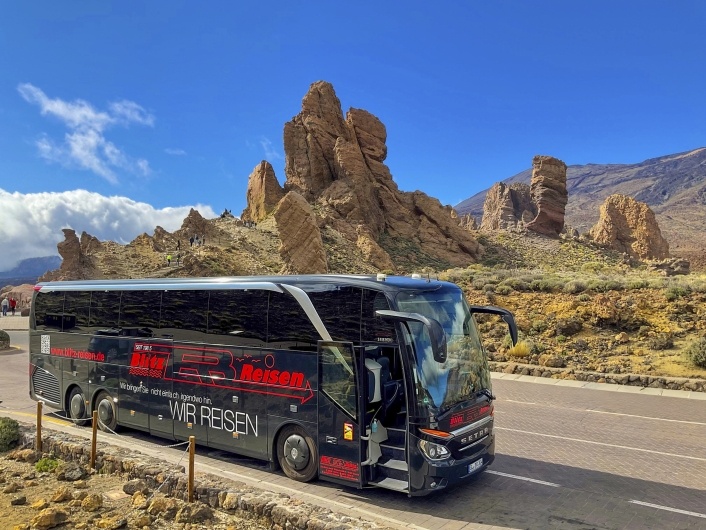 Schwarzer Bus vor orange-gelben Felsen unter blauem Himmel
