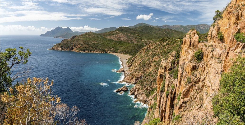 Orange Felsen mit grünen Bäumen und blaues Meer in der Bucht