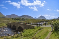 Steinbrücke mit Menschen auf grüner Ebene mit Fluss und Bergen und blauem Himmel