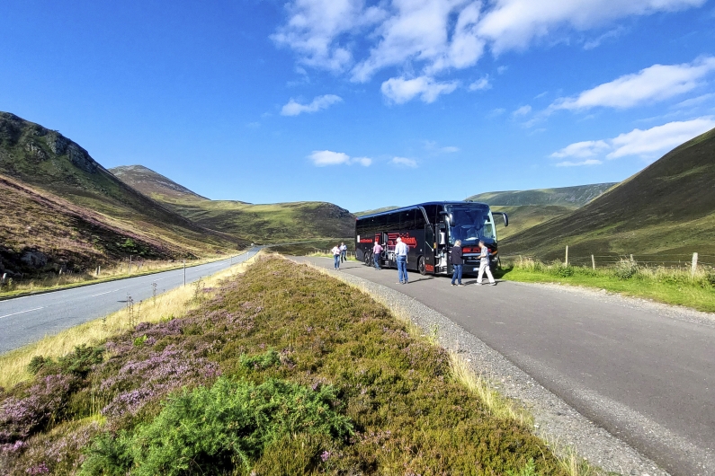 Blauer Himmel und grüne Landschaft mit schwarzen Bus und Reisegästen