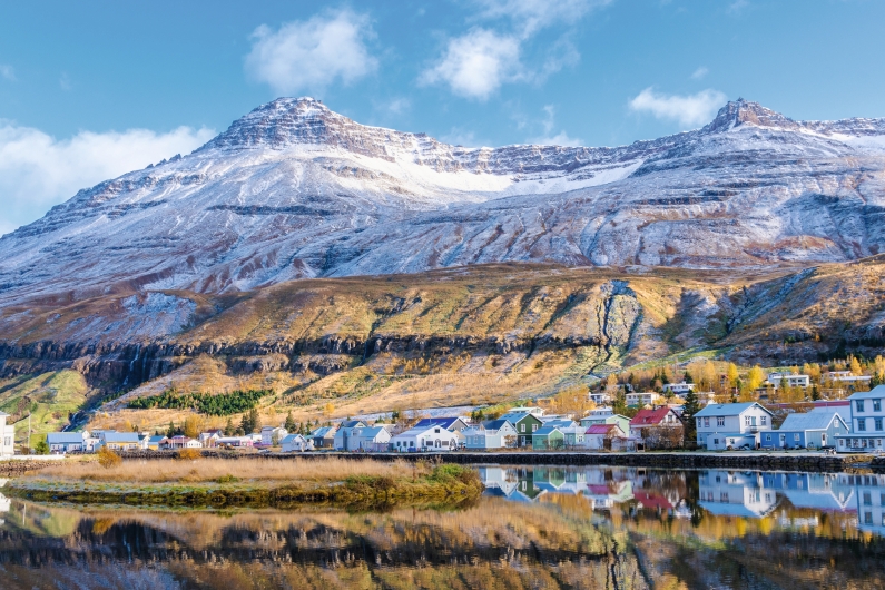 Eine malerische Berglandschaft mit Häusern am Ufer und Herbstbäumen.