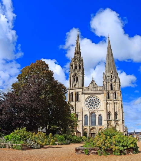 Gotische Kathedrale mit zwei Türmen und Rosettenfenster vor blauem Himmel.