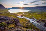 Sonnenuntergang über einem Fjord mit Fluss und grüner Landschaft.