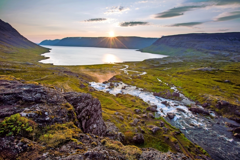 Sonnenuntergang über einem Fjord mit Fluss und grüner Landschaft.